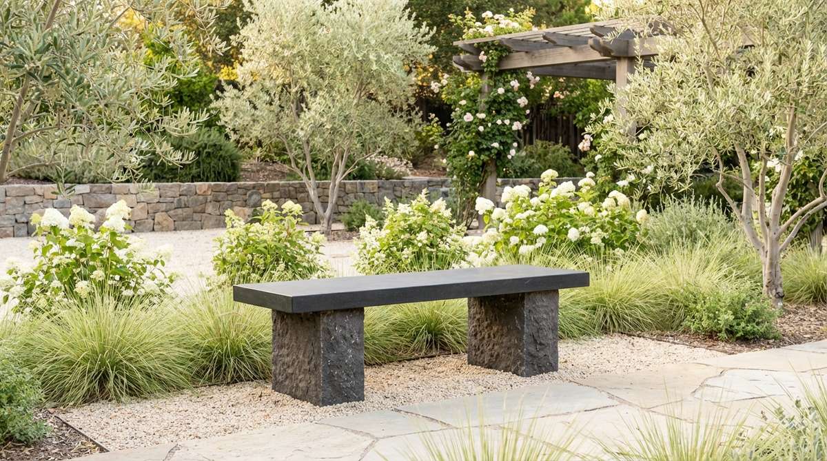 A dark basalt garden bench with a honed satin finish, featuring dense volcanic stone columns that provide striking visual contrast in light-colored gardens. This linear bench absorbs solar heat for cooler climates while remaining cool in shaded areas.